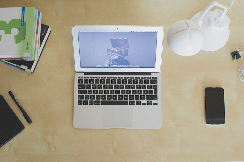 Imagem de um notebook sobre uma mesa, acompanhado por um smartphone, cadernos e uma caneta ao seu redor.